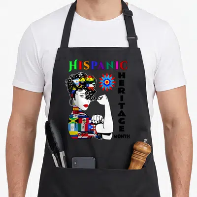 Month country apron - Cartoon woman made of flags flexing arm next to stacked HISPANIC HERITAGE MONTH text — shown on a black cotton canvas apron against a white background