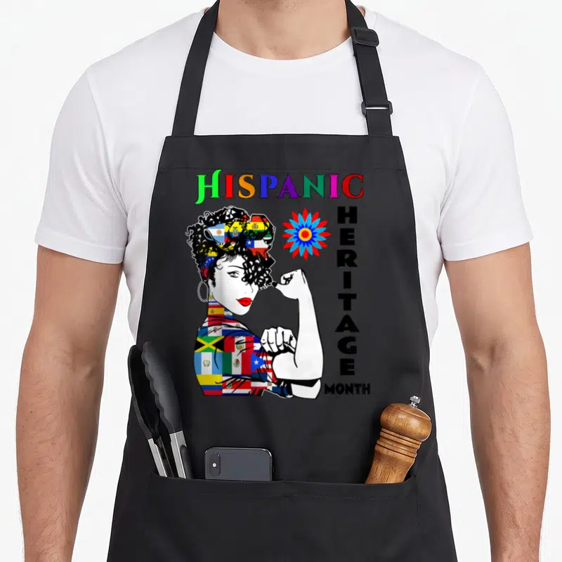 Month country apron - Cartoon woman made of flags flexing arm next to stacked HISPANIC HERITAGE MONTH text — shown on a black cotton canvas apron against a white background