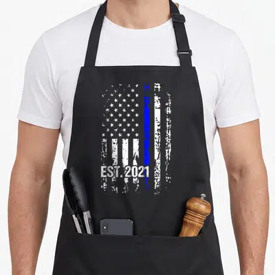 Exam police apron - Vertical distressed American flag with thin blue line and EST.2021 text at bottom — shown on a black cotton canvas apron against a white background