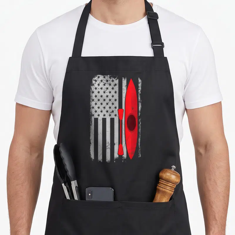 Kayak american flag apron - Red kayak and paddle over distressed grey and white flag pattern — shown on a black cotton canvas apron against a white background