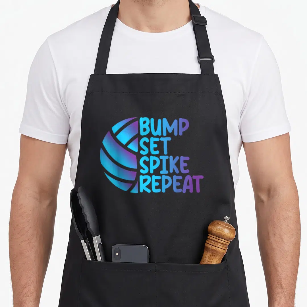 Volleyball bump apron - Stylized ball in blue and purple next to stacked text BUMP SET SPIKE REPEAT — shown on a black cotton canvas apron against a white background