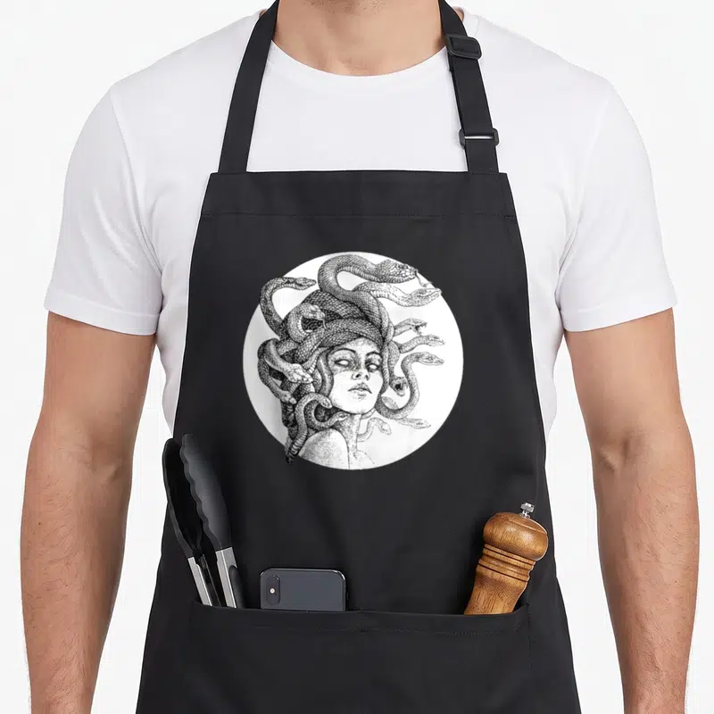 Medusa gothic apron - Black and white line art of Medusa with snakes inside a white circle — shown on a black cotton canvas apron against a white background