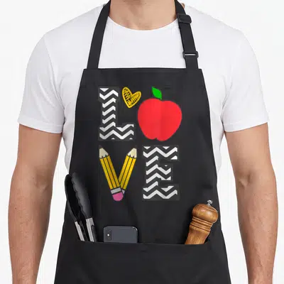 Teaching school teacher apron - LOVE text made of chevron L, heart, red apple, two pencils, and chevron E — shown on a black cotton canvas apron against a white background