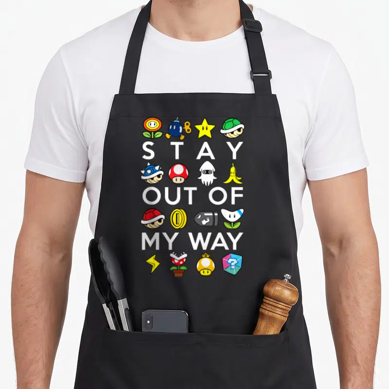 Way stay apron - STAY OUT OF MY WAY text surrounded by rows of game items in red yellow blue green and white — shown on a black cotton canvas apron against a white background
