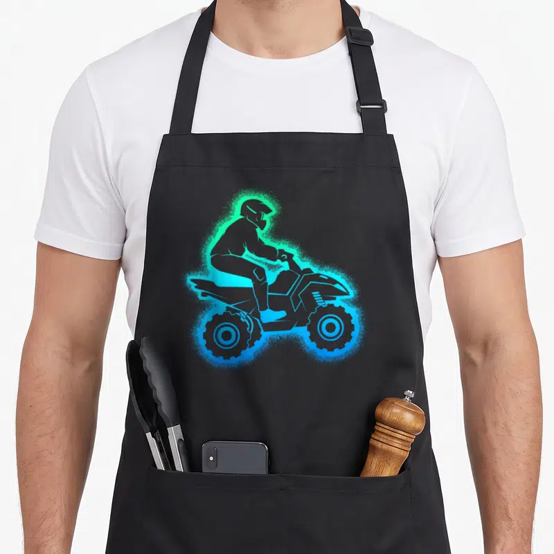 Funny wheeler atv apron - Minimalist silhouette of an ATV rider surrounded by a glowing blue and green spray effect — shown on a black cotton canvas apron against a white background