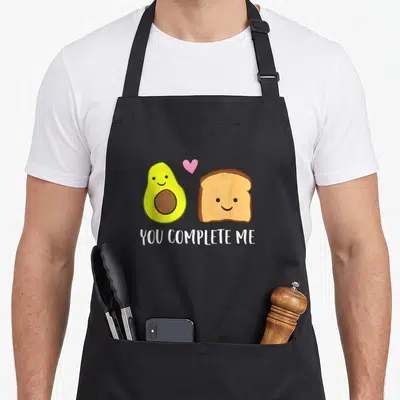Complete toast apron - Smiling avocado and toast with pink heart and white text — shown on a black cotton canvas apron against a white background