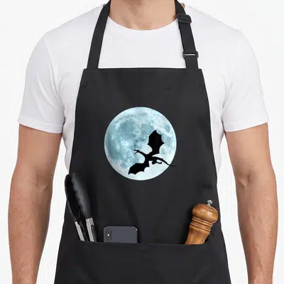 Dragon flying apron - Black dragon silhouette flying across a textured light blue full moon circle — shown on a black cotton canvas apron against a white background