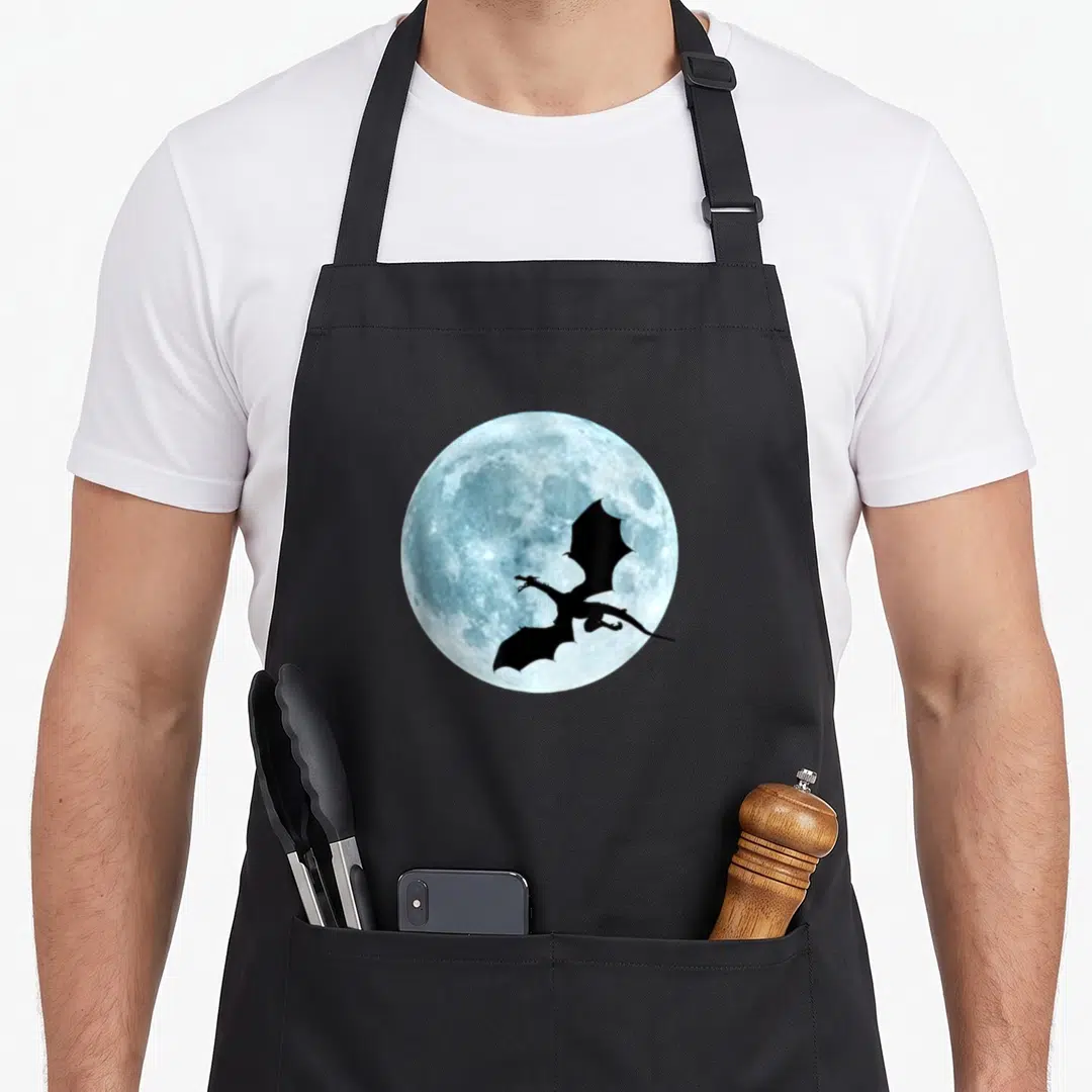 Dragon flying apron - Black dragon silhouette flying across a textured light blue full moon circle — shown on a black cotton canvas apron against a white background