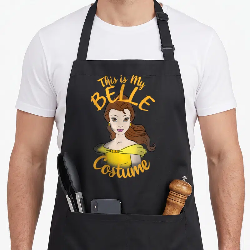 Belle halloween apron - Cartoon Belle in yellow dress with This is My BELLE Costume text in orange and brown — shown on a black cotton canvas apron against a white background