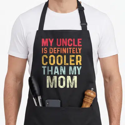 Definitely nephew apron - Stacked red orange yellow blue and white distressed text reading MY UNCLE IS DEFINITELY — shown on a black cotton canvas apron against a white background