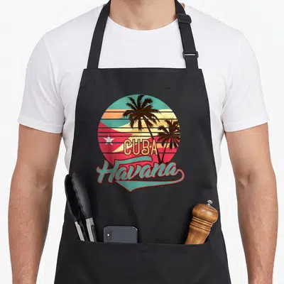 Cuba tree apron - Retro circular print with Cuban flag, palm trees, CUBA text, and Havana script in red teal yellow — shown on a black cotton canvas apron against a white background