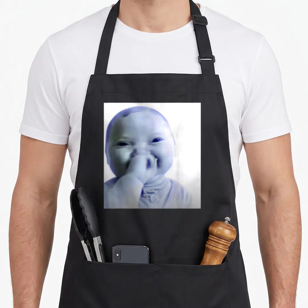 Baby meme apron - Square photo of a smiling baby in blue and white tones centered on fabric — shown on a black cotton canvas apron against a white background