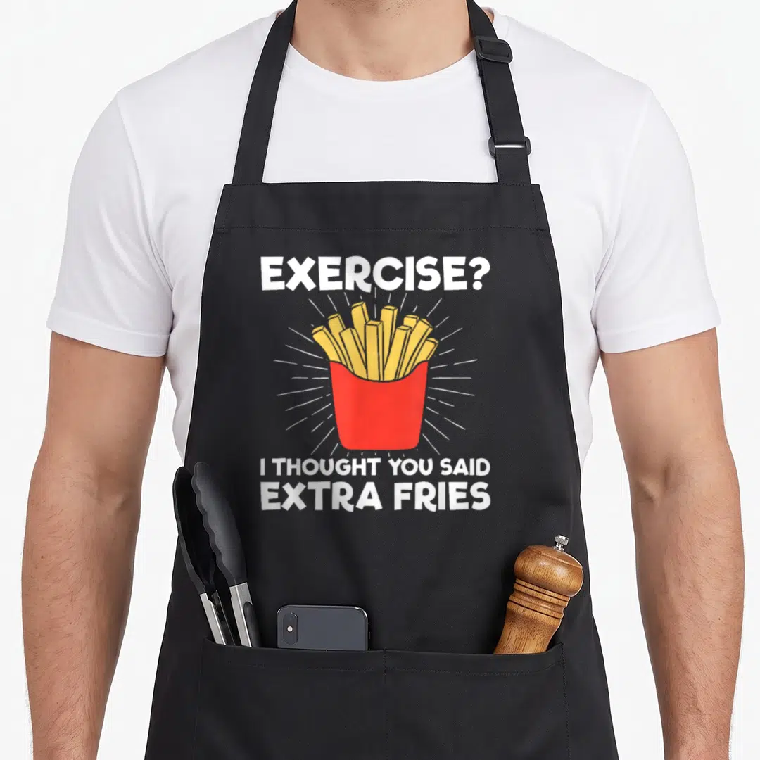 Workout an extra apron - Cartoon red fry box with yellow fries, white rays, and text EXERCISE? I THOUGHT YOU SAID EXTRA — shown on a black cotton canvas apron against a white background