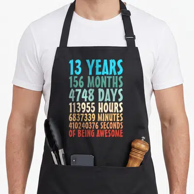 13th countdown birthday apron - Stacked colorful text listing 13 years, 156 months, and seconds of being awesome — shown on a black cotton canvas apron against a white background