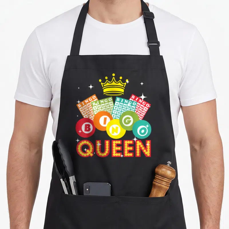 Casino bingo apron - Yellow crown above four colored bingo cards, five lettered chips, and QUEEN text — shown on a black cotton canvas apron against a white background
