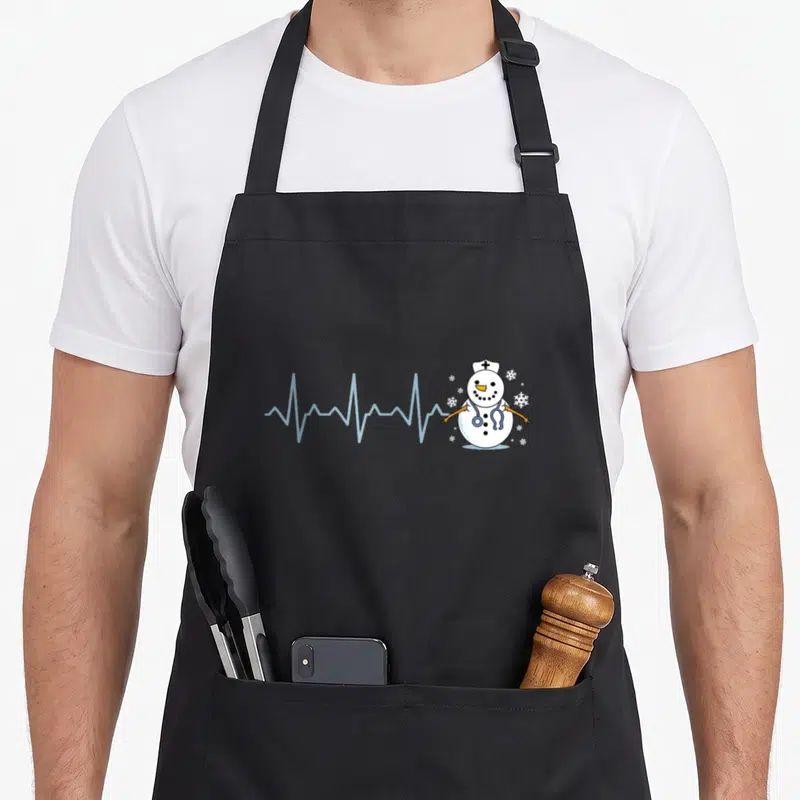 Heartbeat snowman apron - Cartoon nurse snowman with light blue heartbeat line and white snowflakes — shown on a black cotton canvas apron against a white background