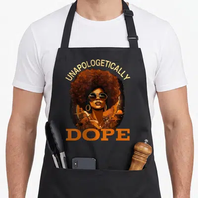 Unapologetically black history apron - Retro woman portrait with arched UNAPOLOGETICALLY text and DOPE below, cityscape — shown on a black cotton canvas apron against a white background