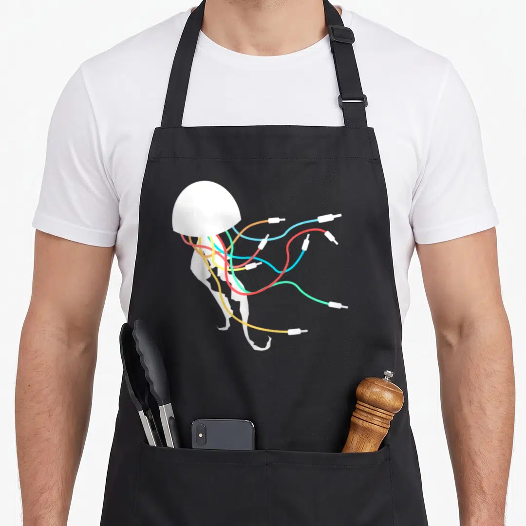 Synthesist jellyfish apron - White jellyfish with orange, yellow, red, blue, and green cable tentacles ending in white — shown on a black cotton canvas apron against a white background