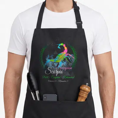 Scorpion birthday apron - Rainbow scorpion in blue, green, pink, yellow with Scorpio text and green circular border — shown on a black cotton canvas apron against a white background