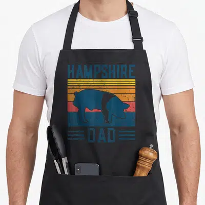 Hampshire farming apron - Retro pig silhouette over blue yellow orange and red stripes with HAMPSHIRE DAD text — shown on a black cotton canvas apron against a white background