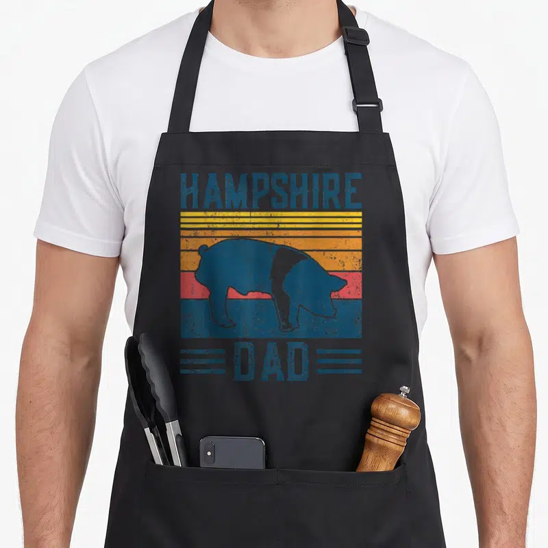 Hampshire farming apron - Retro pig silhouette over blue yellow orange and red stripes with HAMPSHIRE DAD text — shown on a black cotton canvas apron against a white background