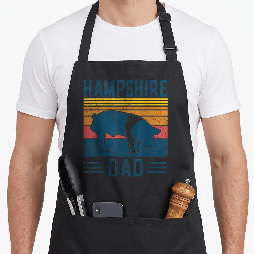 Hampshire farming apron - Retro pig silhouette over blue yellow orange and red stripes with HAMPSHIRE DAD text — shown on a black cotton canvas apron against a white background