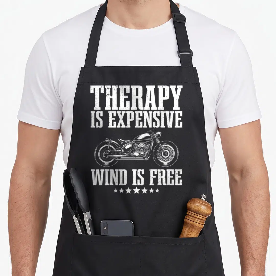 Motorcycle rider bike apron - White distressed text Therapy Is Expensive Wind Is Free with motorcycle and stars — shown on a black cotton canvas apron against a white background
