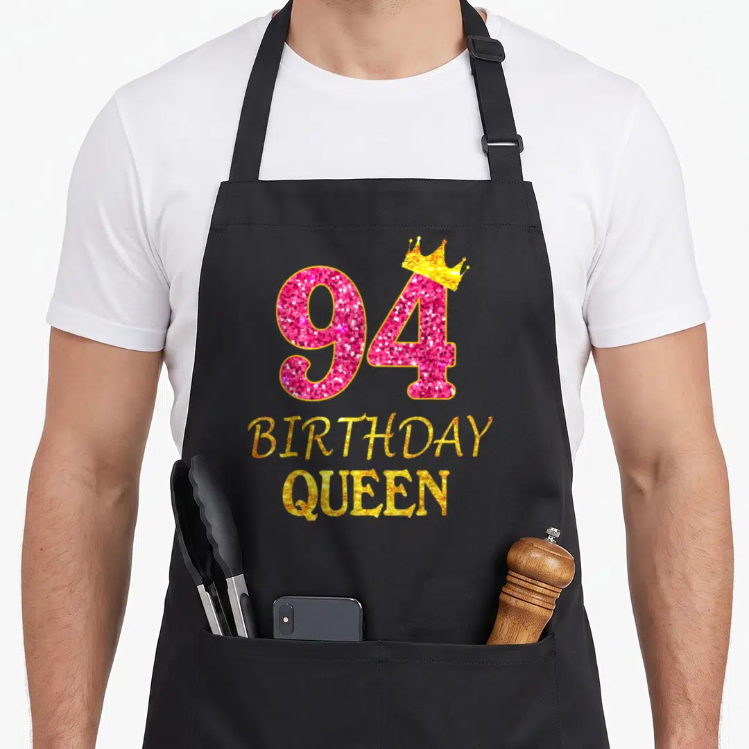 Crown birthday queen of baking apron - Pink glitter number 94 with gold crown and stacked BIRTHDAY QUEEN text — shown on a black cotton canvas apron against a white background