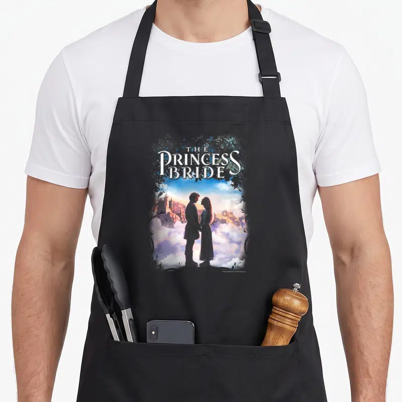 Storybook princess apron - The Princess Bride text above couple silhouette against castle and clouds — shown on a black cotton canvas apron against a white background