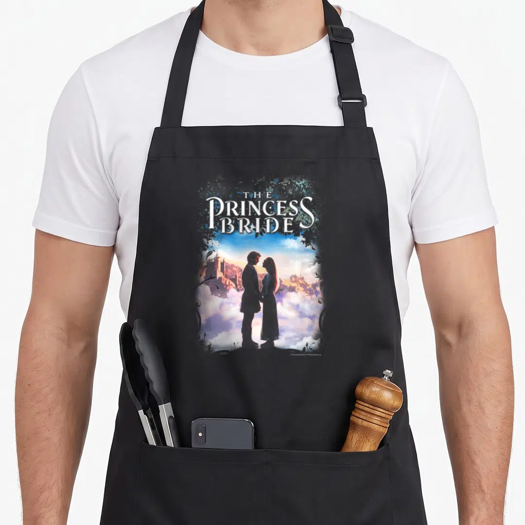 Storybook princess apron - The Princess Bride text above couple silhouette against castle and clouds — shown on a black cotton canvas apron against a white background