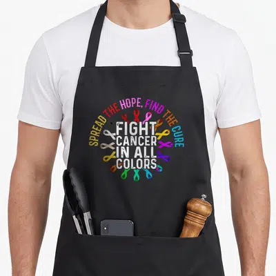 Fight cancer ribbon apron - Multicolored awareness ribbons surrounding white text reading SPREAD THE HOPE FIND THE CURE — shown on a black cotton canvas apron against a white background