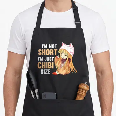 Chibi kawaii anime apron - Stacked orange and white text next to blonde anime girl wearing cat hat — shown on a black cotton canvas apron against a white background