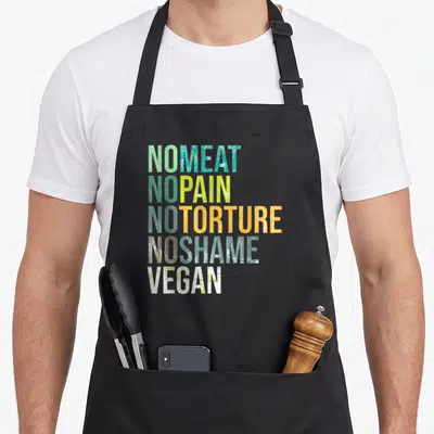 Meat plant based apron - Stacked text NO MEAT NO PAIN NO TORTURE NO SHAME VEGAN in green teal orange white grunge font — shown on a black cotton canvas apron against a white background