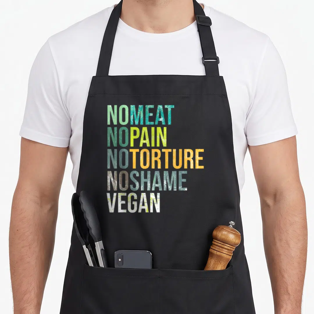 Meat plant based apron - Stacked text NO MEAT NO PAIN NO TORTURE NO SHAME VEGAN in green teal orange white grunge font — shown on a black cotton canvas apron against a white background