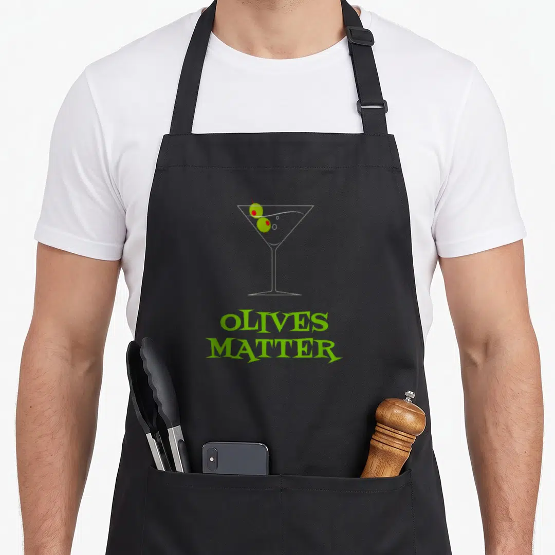 Martini cosmopolitan apron - Minimalist martini glass with two green olives and red picks above stacked green text — shown on a black cotton canvas apron against a white background