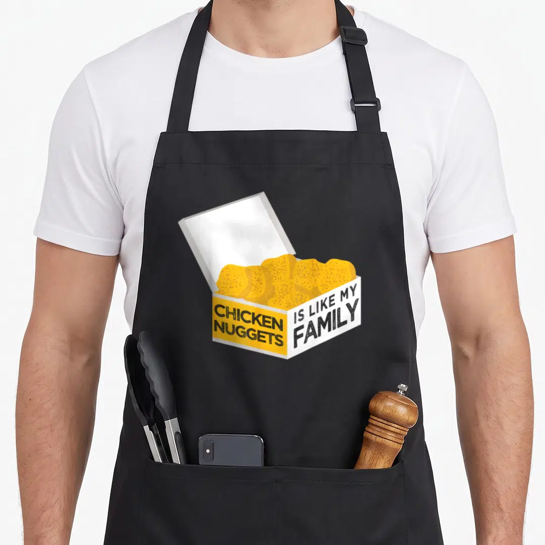 Nugget family chicken apron - Open yellow and white box filled with chicken nuggets and black text reading CHICKEN — shown on a black cotton canvas apron against a white background