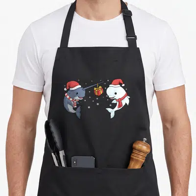 Narwhal christmas apron - Cartoon narwhal giving a red gift to a beluga whale wearing santa hats and snowflakes — shown on a black cotton canvas apron against a white background