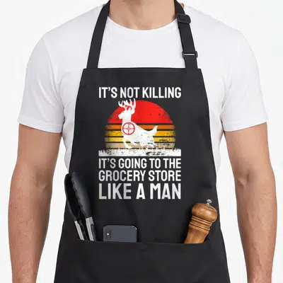 Wild grill hunter apron - White deer silhouette with red crosshair in front of striped retro sun and grocery store quote — shown on a black cotton canvas apron against a white background