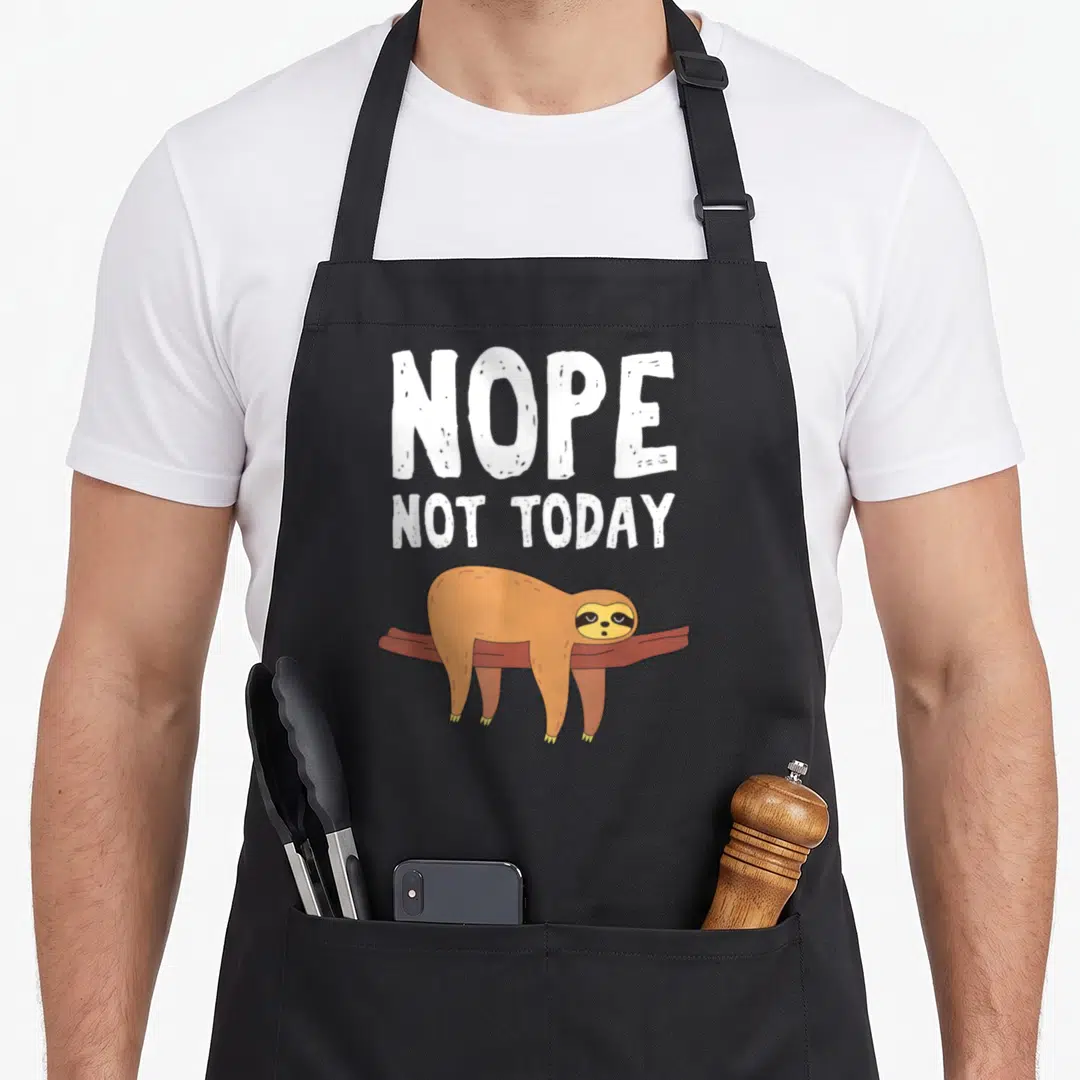 Nope today sloth apron - White nope not today text above brown cartoon sloth lying on branch — shown on a black cotton canvas apron against a white background