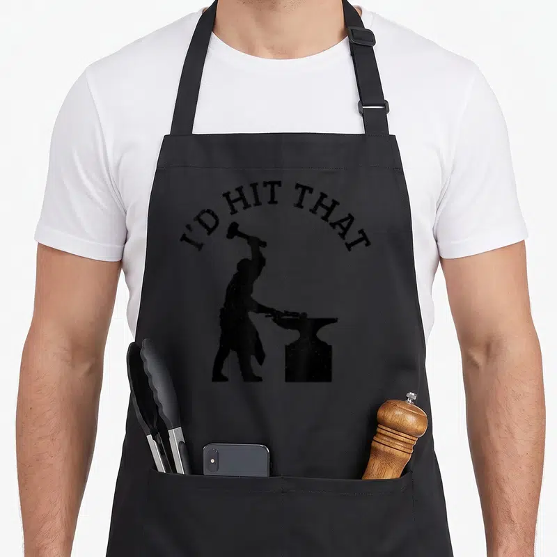 Vintage blacksmith apron - I'D HIT THAT text over blacksmith silhouette hammering anvil, distressed black print — shown on a black cotton canvas apron against a white background