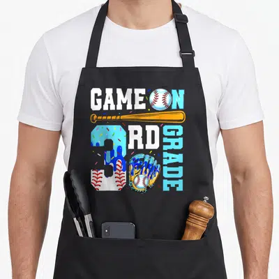 3rd drip apron - Game On 3rd Grade text with baseball, orange bat, blue dripping number 3 with sprinkles, and glove — shown on a black cotton canvas apron against a white background