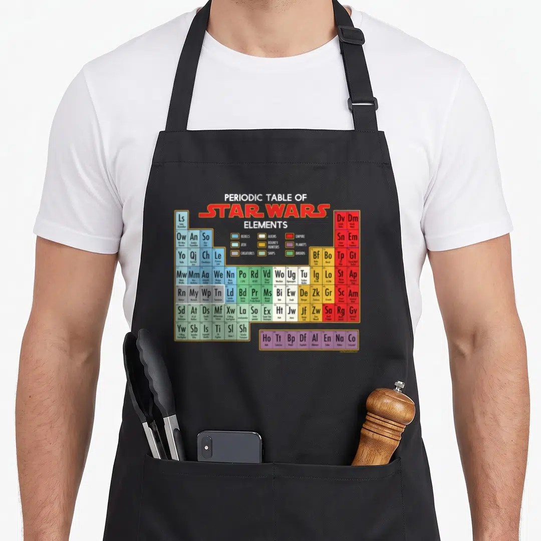 Element table apron - Star Wars periodic table grid with colored cells listing characters ships and planets — shown on a black cotton canvas apron against a white background
