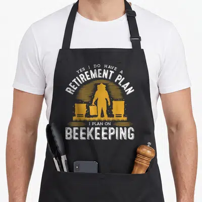Retirement bee apron - White arched text Yes I Do Have A Retirement Plan over yellow beekeeper silhouette flanked — shown on a black cotton canvas apron against a white background