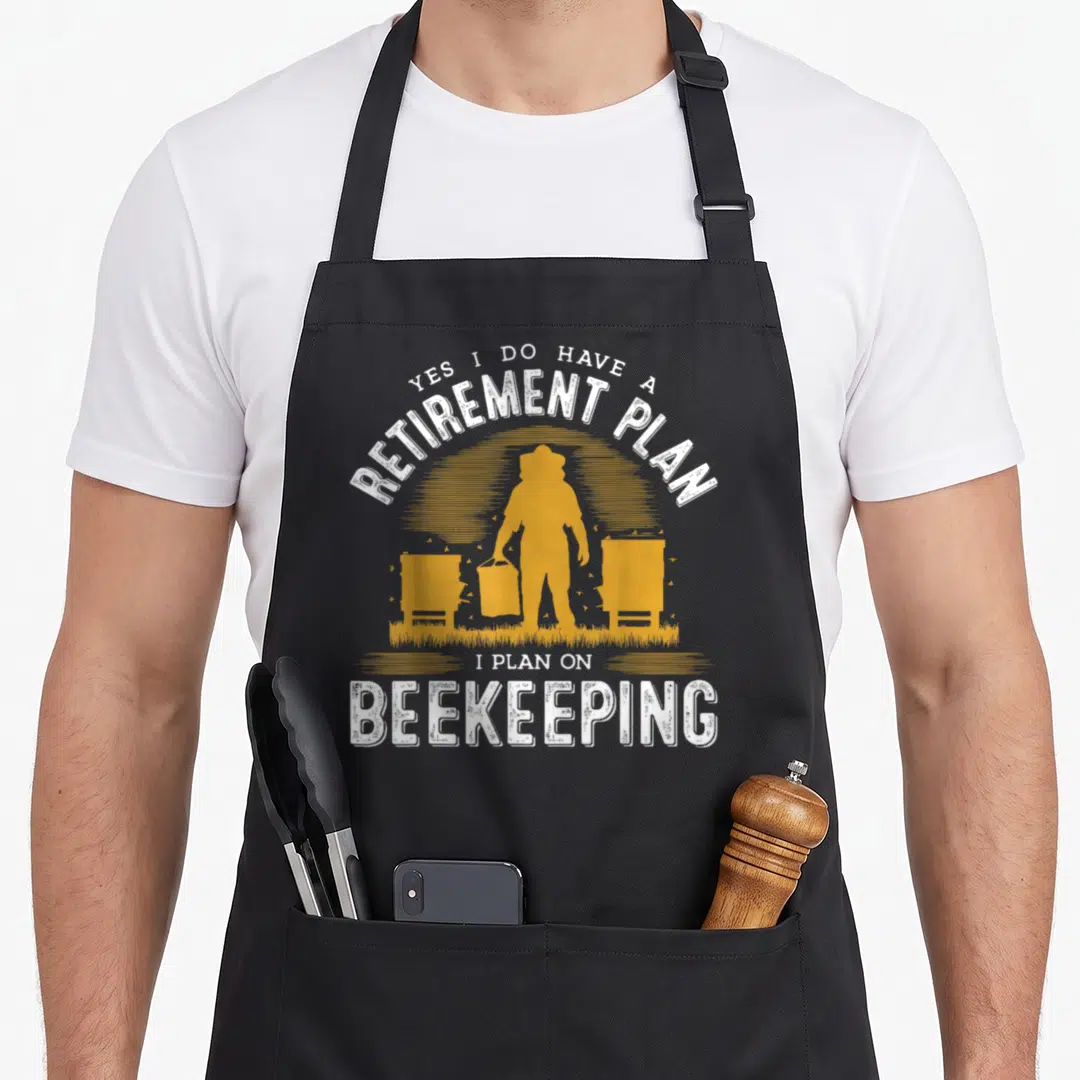 Retirement bee apron - White arched text Yes I Do Have A Retirement Plan over yellow beekeeper silhouette flanked — shown on a black cotton canvas apron against a white background