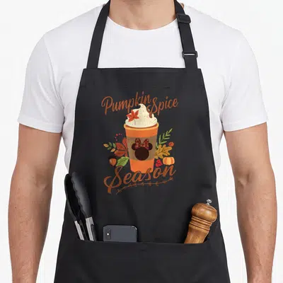Friend spice apron - Coffee cup with whipped cream, Minnie Mouse bow, autumn leaves, pumpkin, acorn, and 'Pumpkin Spice — shown on a black cotton canvas apron against a white background