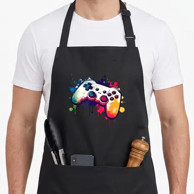 Control controller video game apron - Multicolored cartoon game controller with blue, red, yellow, green, and purple — shown on a black cotton canvas apron against a white background