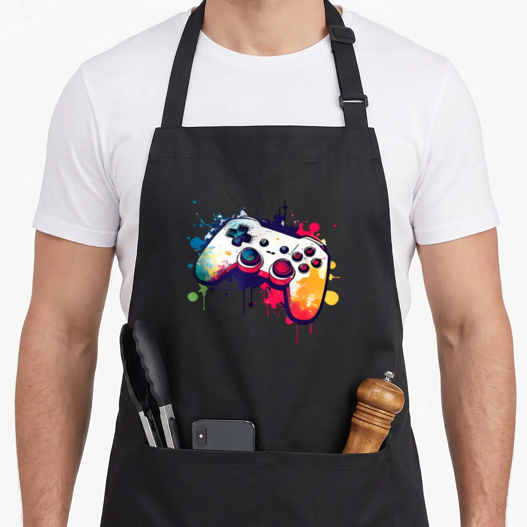 Control controller video game apron - Multicolored cartoon game controller with blue, red, yellow, green, and purple — shown on a black cotton canvas apron against a white background