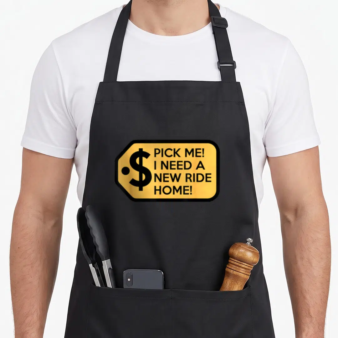 Pick game aprons - Yellow tag with black border, dollar sign, and text PICK ME I NEED A NEW RIDE HOME — shown on a black cotton canvas apron against a white background
