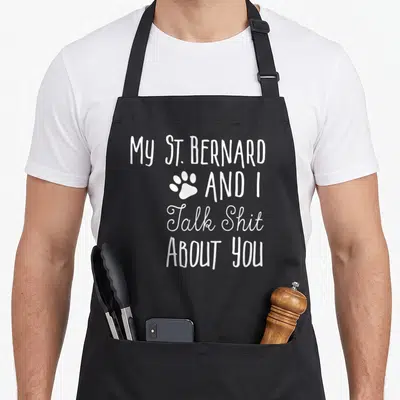 Bernard saint dog apron - White stacked text reading My St. Bernard and I Talk Shit About You with a paw print — shown on a black cotton canvas apron against a white background