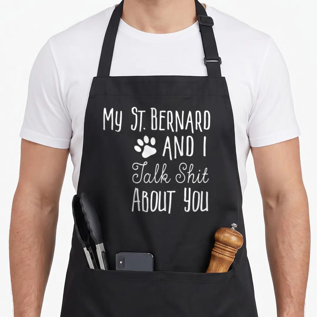 Bernard saint dog apron - White stacked text reading My St. Bernard and I Talk Shit About You with a paw print — shown on a black cotton canvas apron against a white background